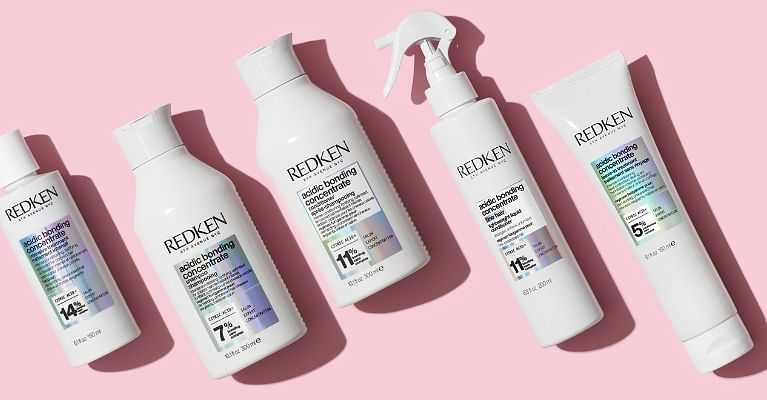 Redken hair care products arranged on a pink background.