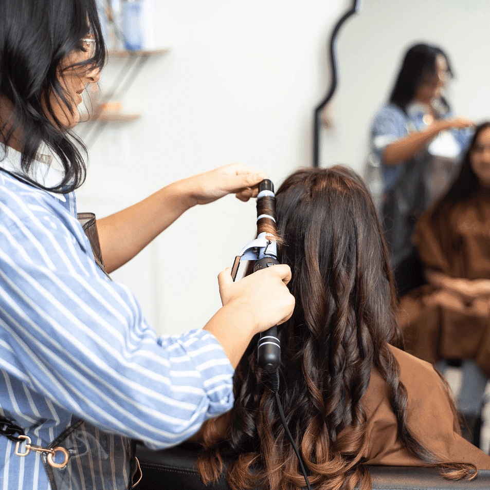 Hairstylist curling a woman's hair in salon.